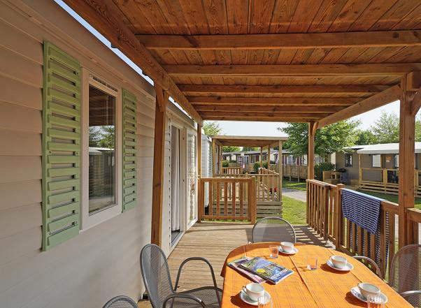 Veranda in legno con tavolo apparecchiato, vista su case mobili.